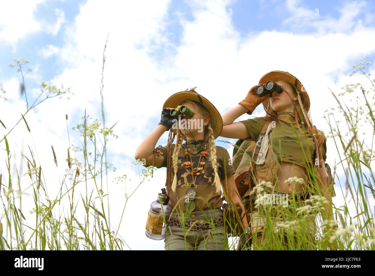Due ragazze giovani sono viste come esploratori. Osservano la campagna all'aperto. Sono vestiti con cappelli safari, binocoli e abiti da safari kaki. Foto Stock
