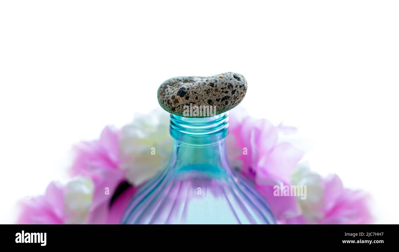 Bottiglia trasparente e blu turchese con pietra come tappo circondata da colori pastello rosa e bianco che rappresentano bellezza e cura personale Foto Stock