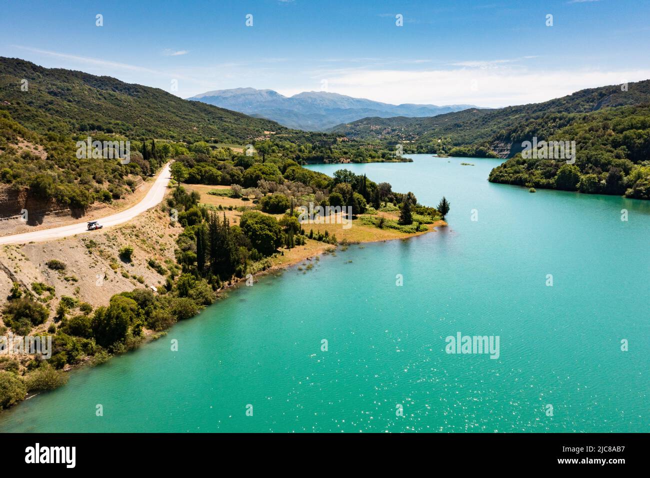 RoadTrip: Vista aerea su un lago blu con strada che si snoda lungo la riva e un parcheggio 4x4 vicino ad esso Foto Stock
