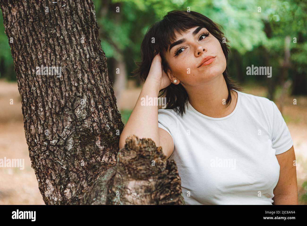 Una giovane ragazza con corti capelli neri, una T-shirt bianca e una gonna nera nel bosco tra alberi verdi e erba verde Foto Stock