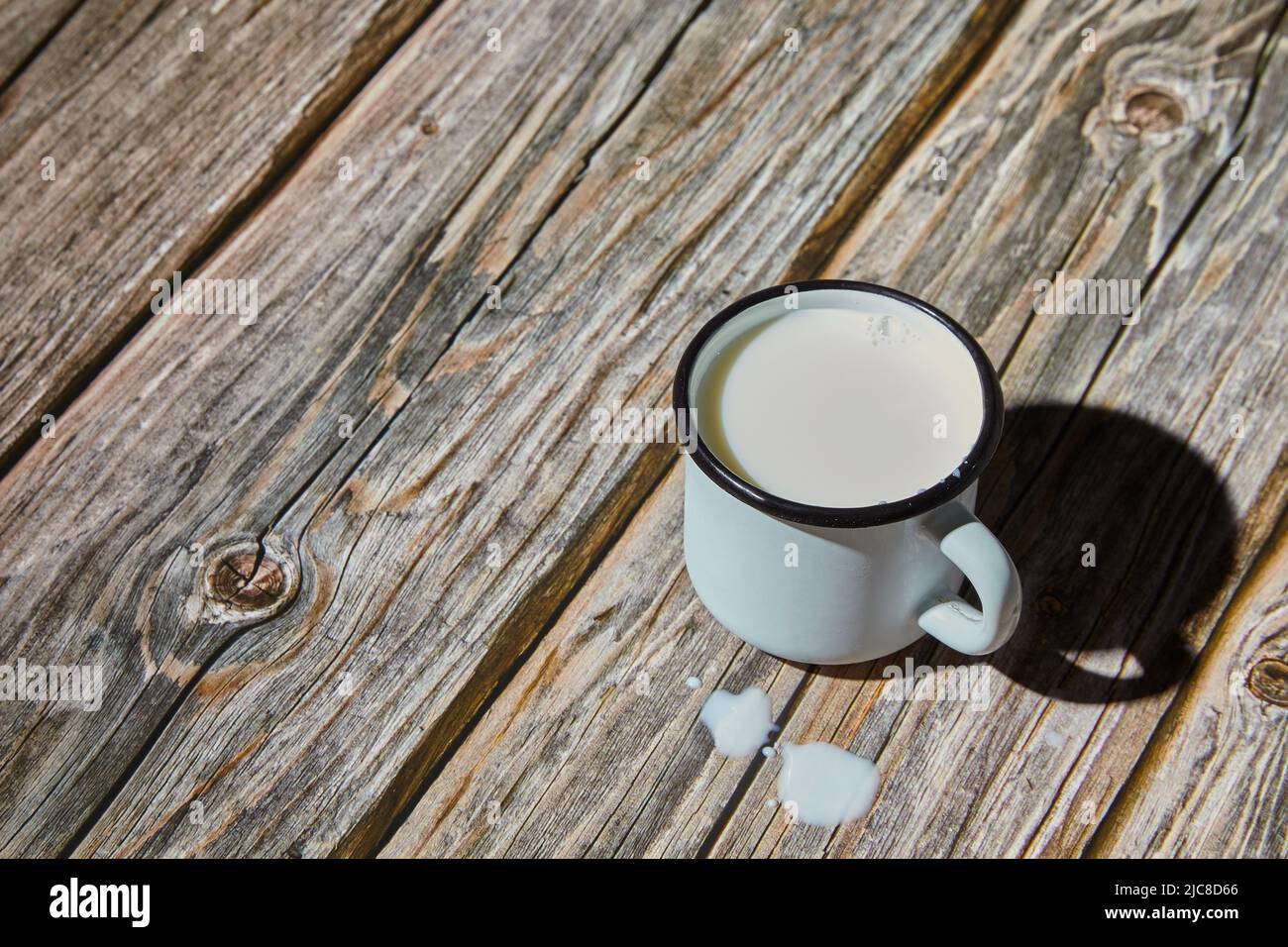 Latte in una tazza blu chiaro smaltata su un tavolo di legno grezzo. Luce del mattino Foto Stock