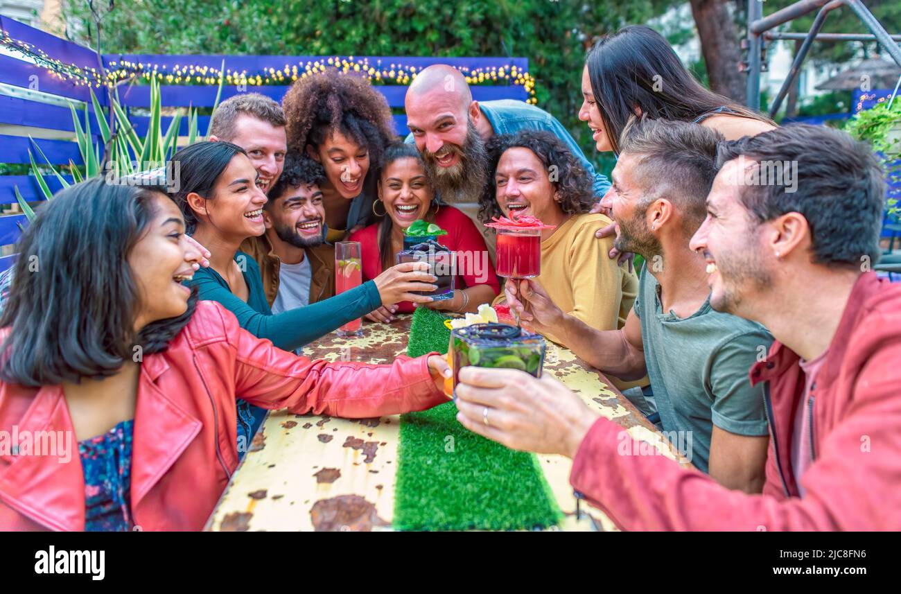 gruppo multietnico di amici seduti su un tavolo in un ristorante lounge bar che prepara toast con un meraviglioso cocktail gourmet. persone diverse che sedano Foto Stock