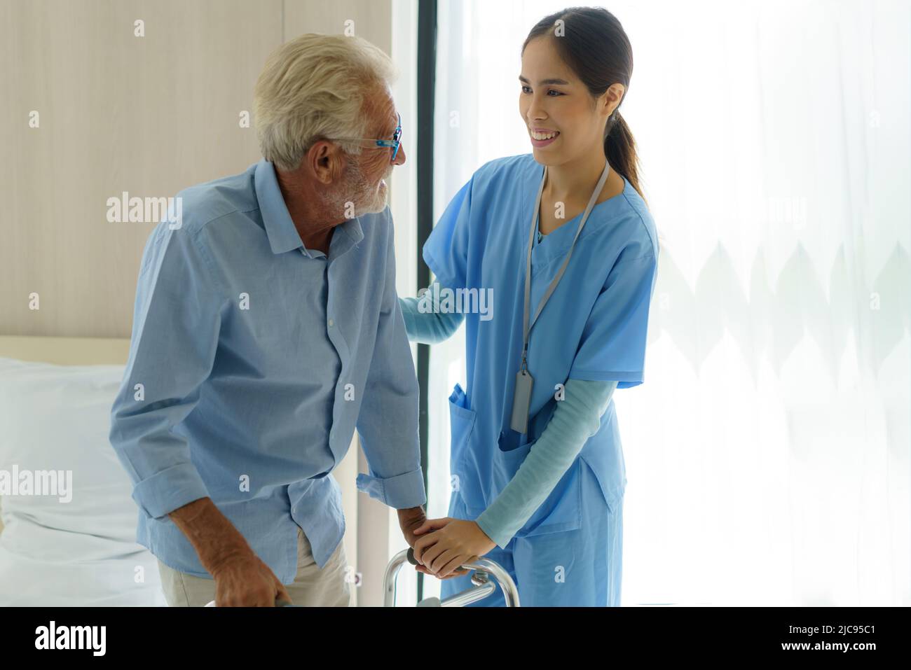 Infermiere sorridente asiatico che aiuta l'uomo anziano a uscire dal letto assistenza infermieristica sostenere il paziente mentre si esce dal letto e si sposta in sedia a rotelle a casa aiutando h Foto Stock