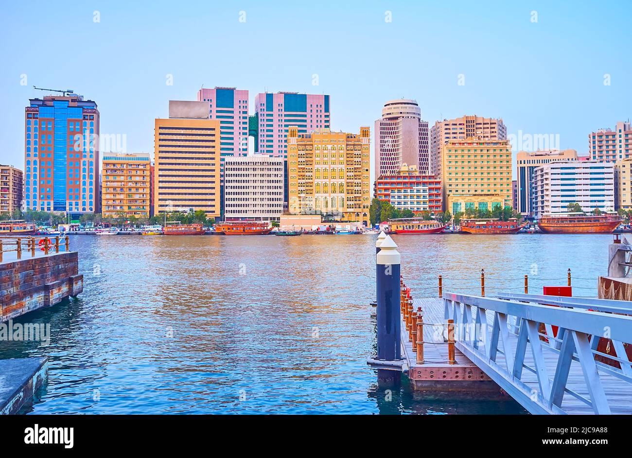 L'argine del quartiere di Deira con linee di edifici moderni e barche in sambuco vintage dietro Dubai Creek, Emirati Arabi Uniti Foto Stock
