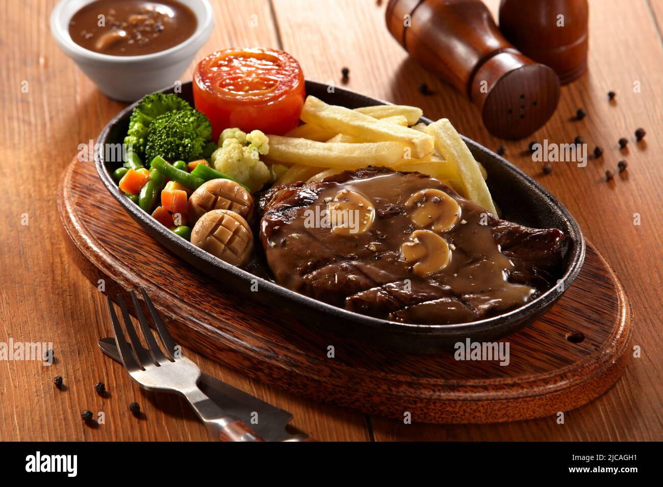 Bistecca di manzo con salsa di funghi al pepe nero servita con patate e verdure su un piatto caldo Foto Stock