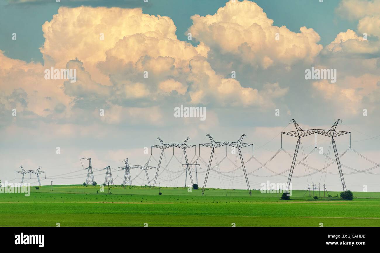 Linee elettriche sul campo di campagna con grandi nuvole sullo sfondo. Concetto di distribuzione dell'energia e dell'energia. Mancanza di energia. Foto Stock