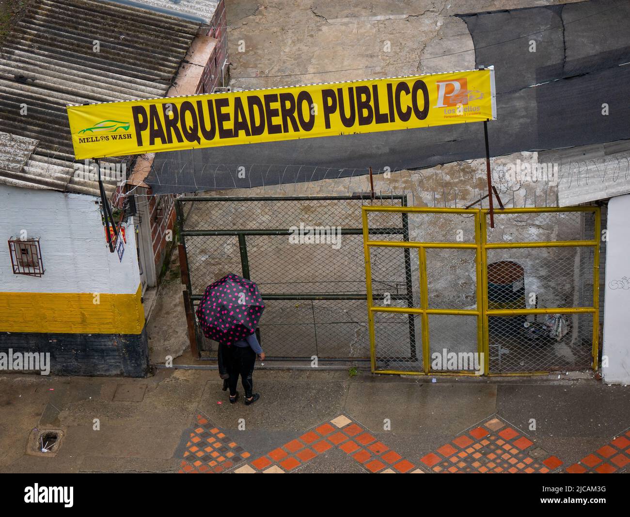 Medellin, Antioquia, Colombia - Marzo 6 2022: Donna con un ombrello nero con punti Fuchsia sta aspettando al cancello sotto un segno giallo che dice 'Pub Foto Stock