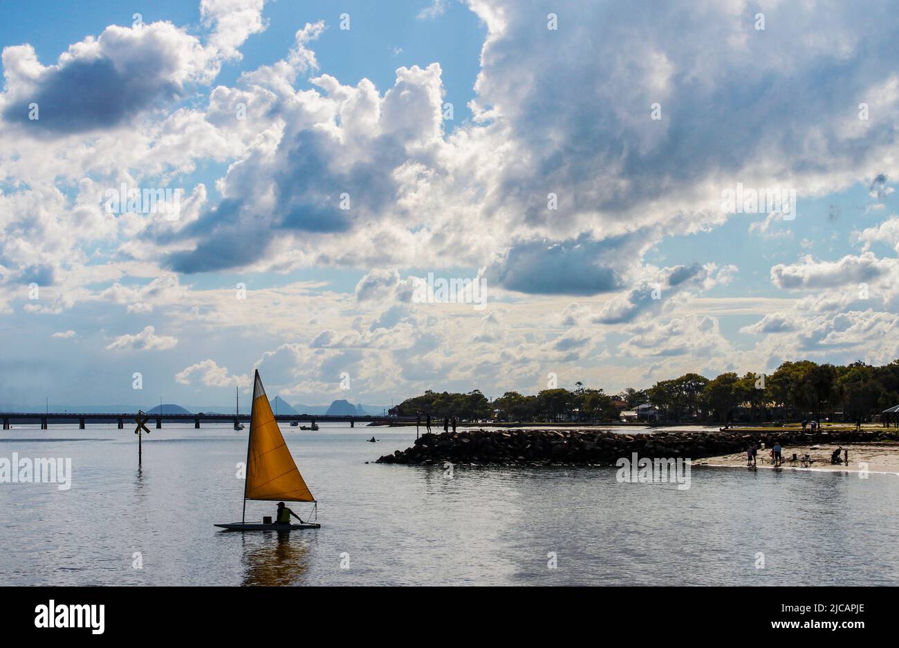 Singlehander vela dinghie al crepuscolo con ponte e montagne in lontananza sotto il cielo drammatico - Isola di Bribie Australia Foto Stock