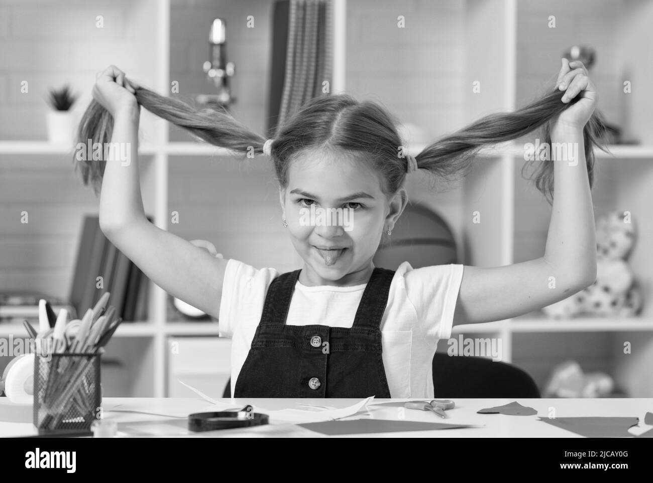 sorridente ragazza teen che si diverte con coda di pony lungo capelli alla lezione di scuola, giorno della conoscenza. Foto Stock