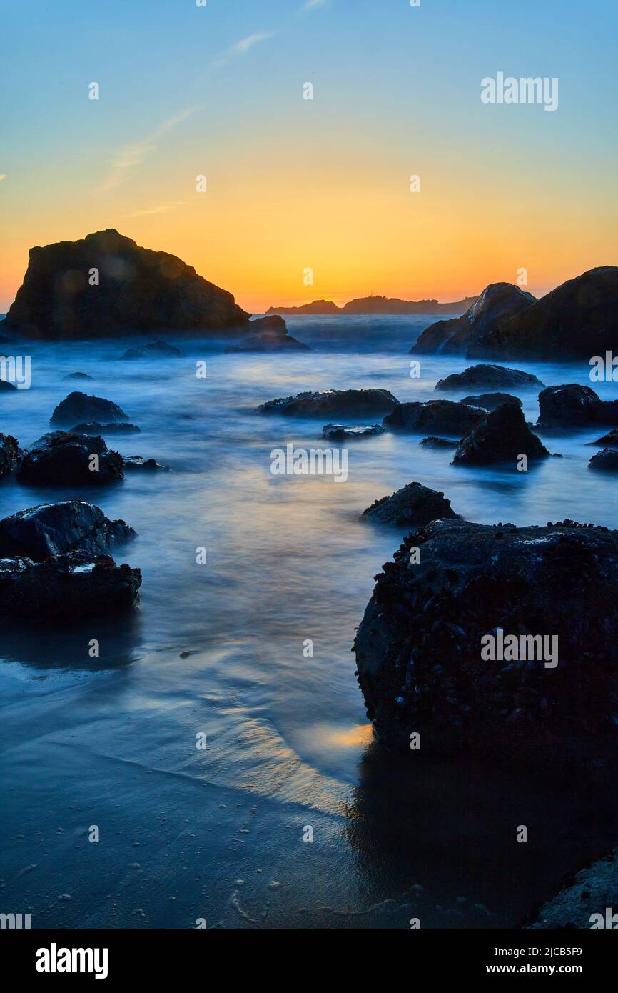 Onde fluide intorno alle rocce sulla spiaggia all'ora d'oro in California Foto Stock