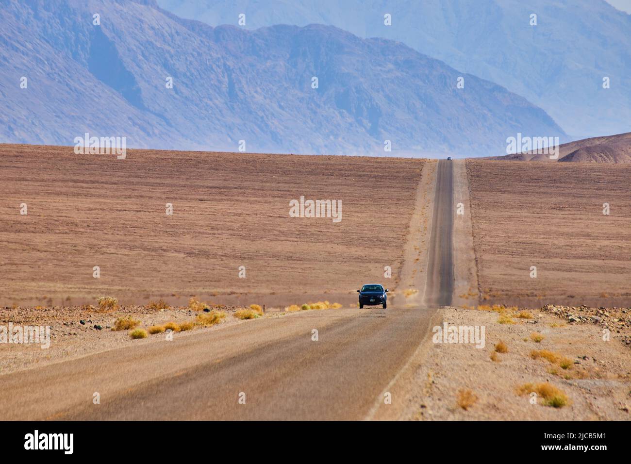 Lunga strada rettilinea con auto che guida attraverso pianure desertiche vuote e colline da montagne Foto Stock