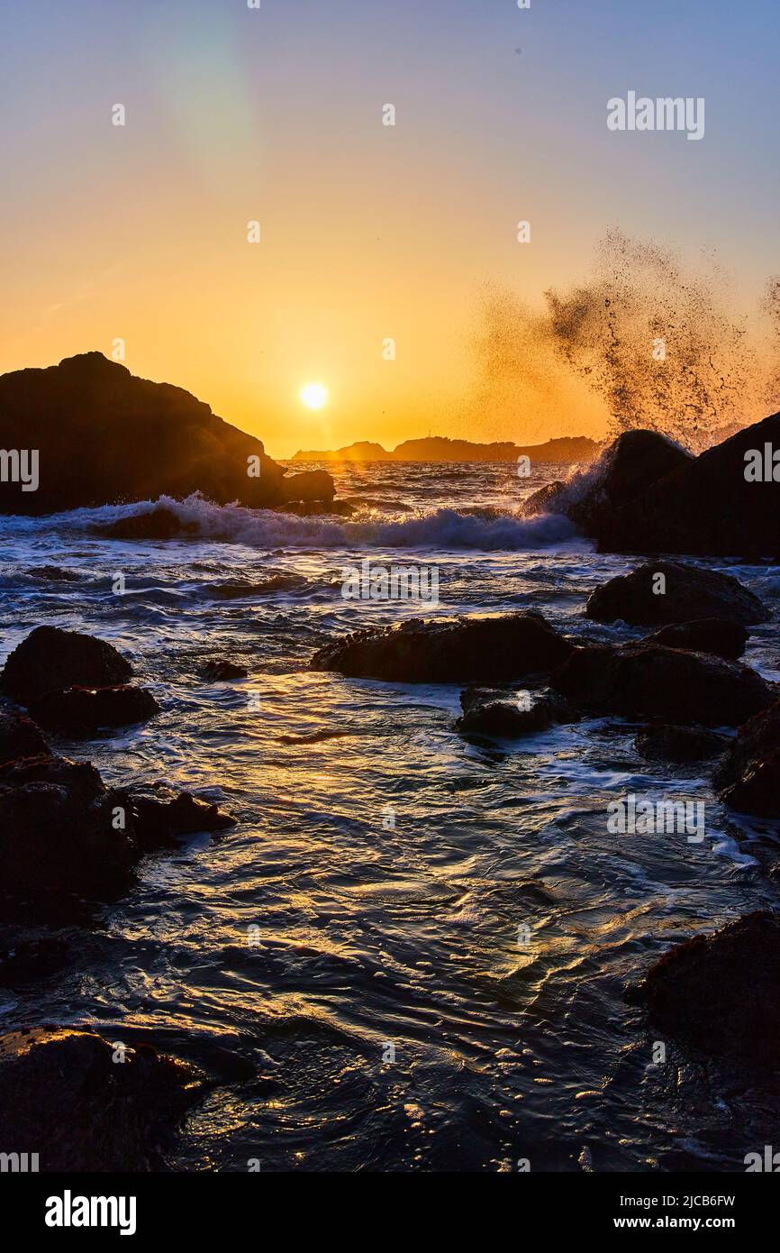Tramonto sulla spiaggia della costa occidentale con onde che si infrangono sulle rocce Foto Stock