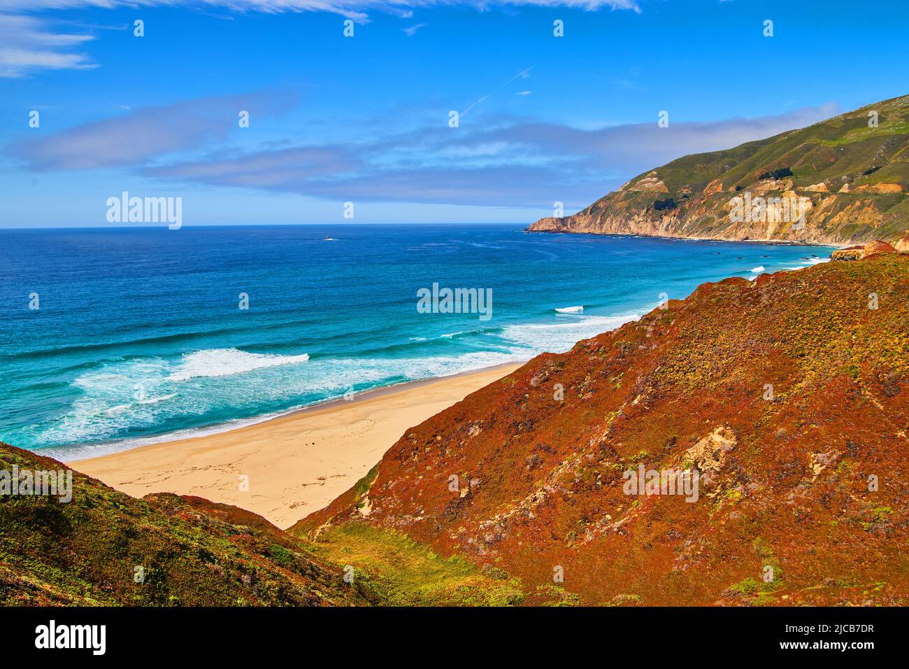 Le tranquille onde dell'oceano colpiscono la spiaggia sabbiosa vicino alle colline di piante rosse e verdi di primavera Foto Stock