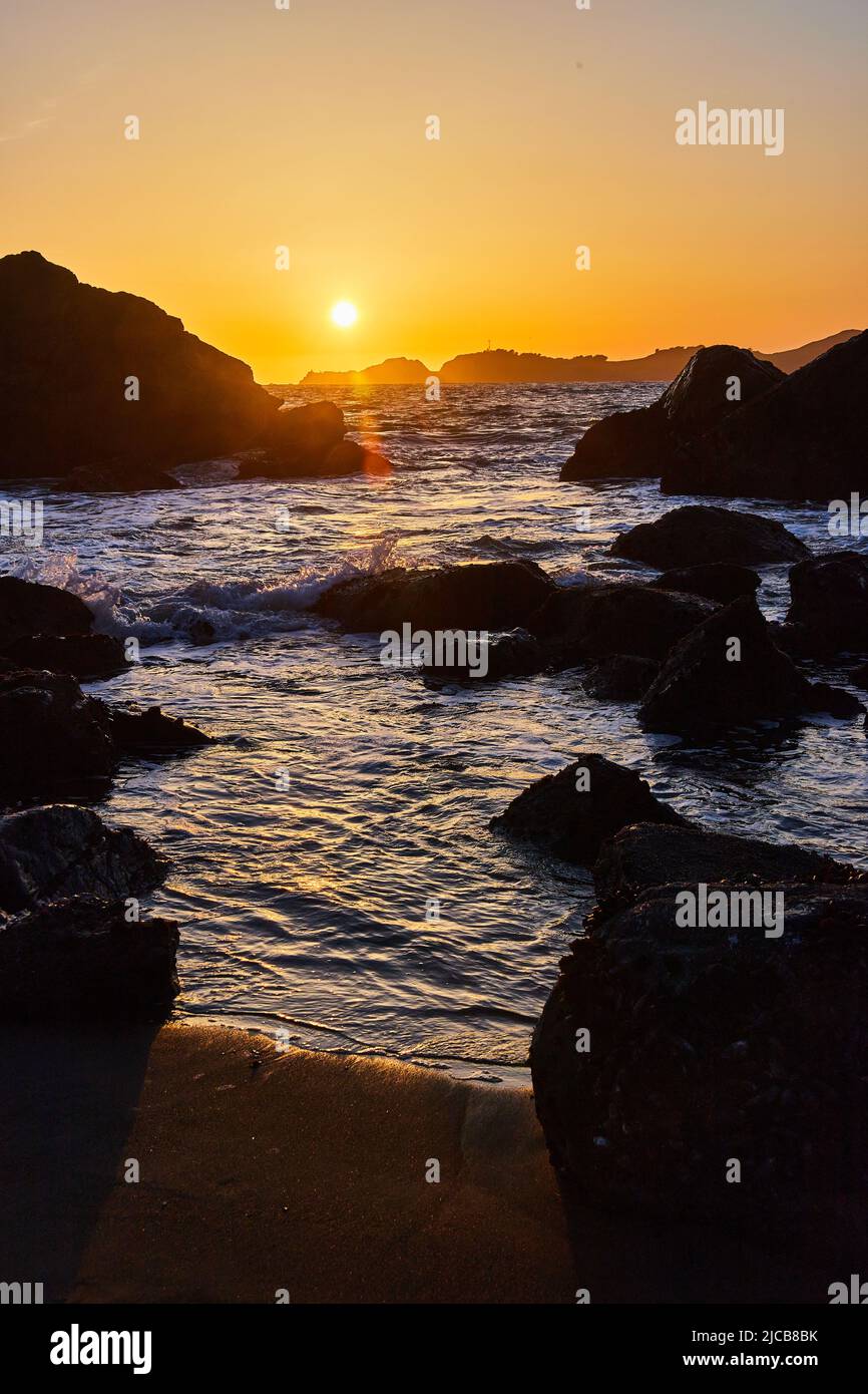 Spiaggia di sabbia con onde sulle rocce vicino al tramonto vibrante Foto Stock