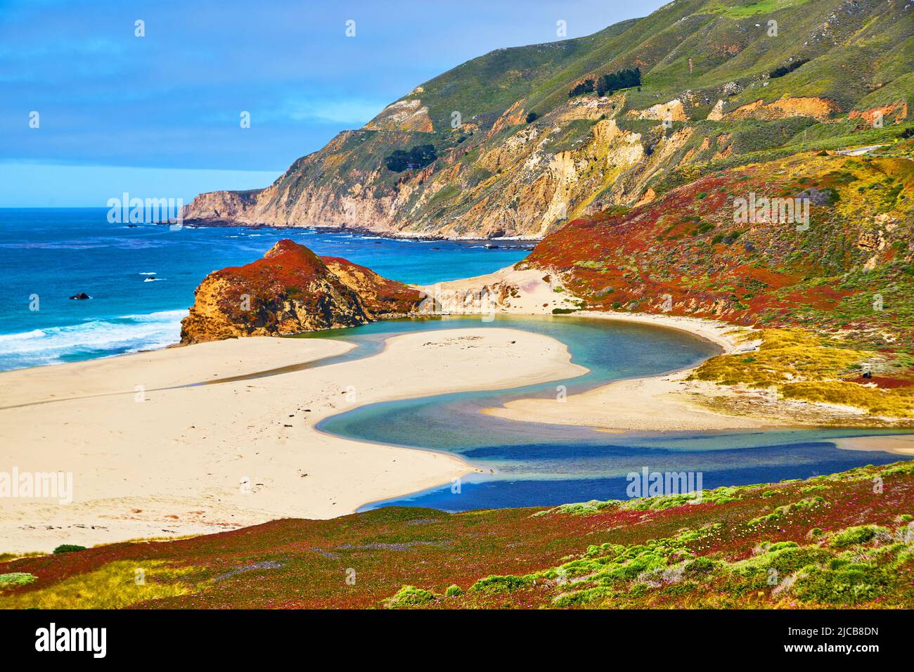 Maestoso fiume blu sulla spiaggia oceano incontra l'oceano circondato da colline coperte di piante primaverili Foto Stock