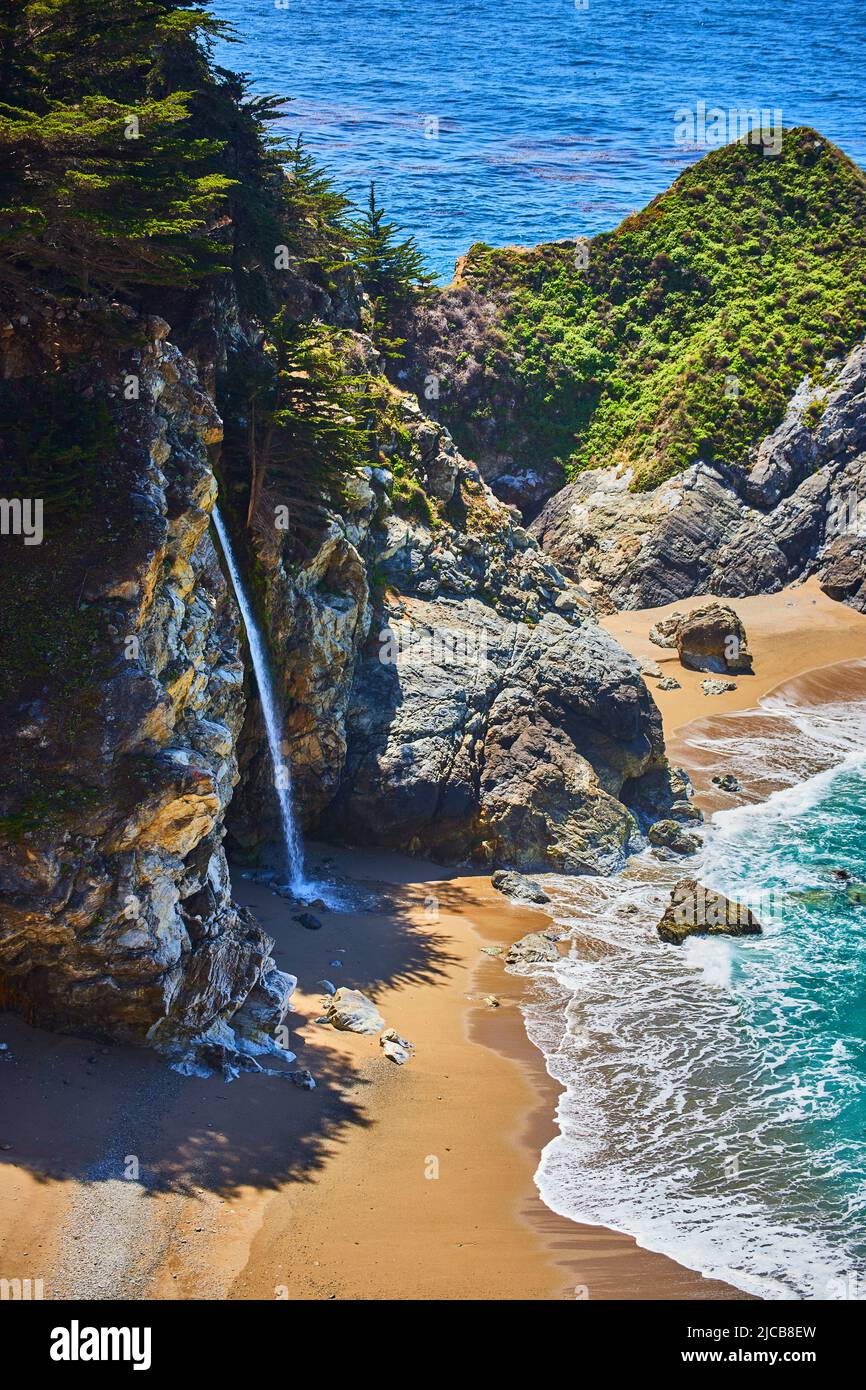 Splendida cascata nascosta che si riversa sulle spiagge sabbiose con le onde dell'oceano che si infrangono nelle vicinanze Foto Stock
