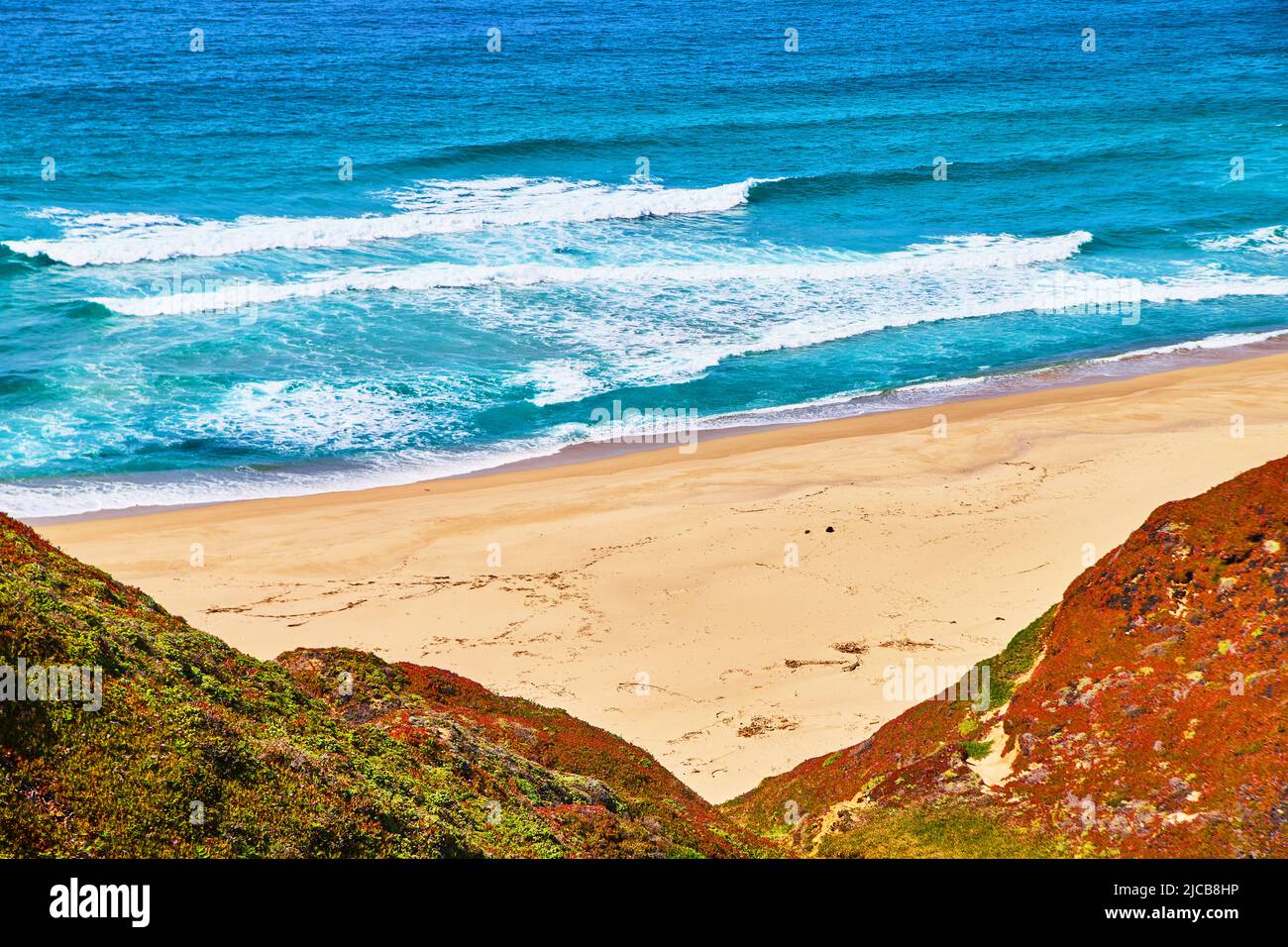 Un'ampia zona di spiagge sabbiose circondata da onde oceaniche e colline di piante primaverili Foto Stock