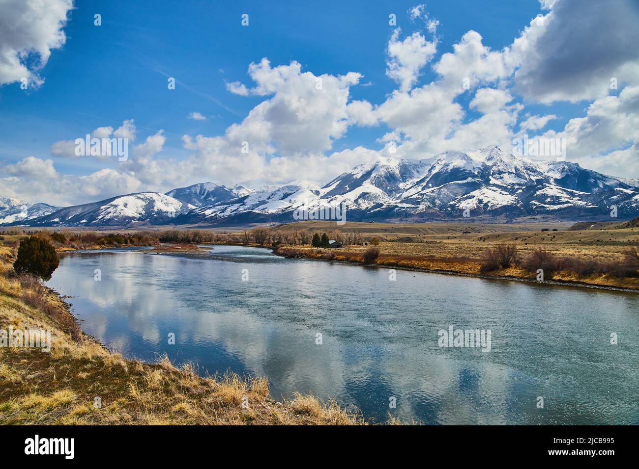 Fiume e campi in primavera con incredibili montagne innevate all'orizzonte Foto Stock