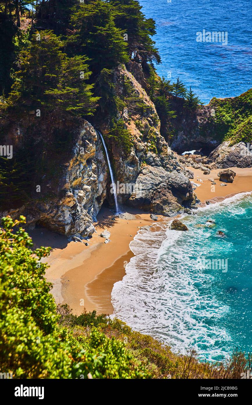 Spiaggia sabbiosa con onde oceaniche e cascata nascosta mozzafiato Foto Stock
