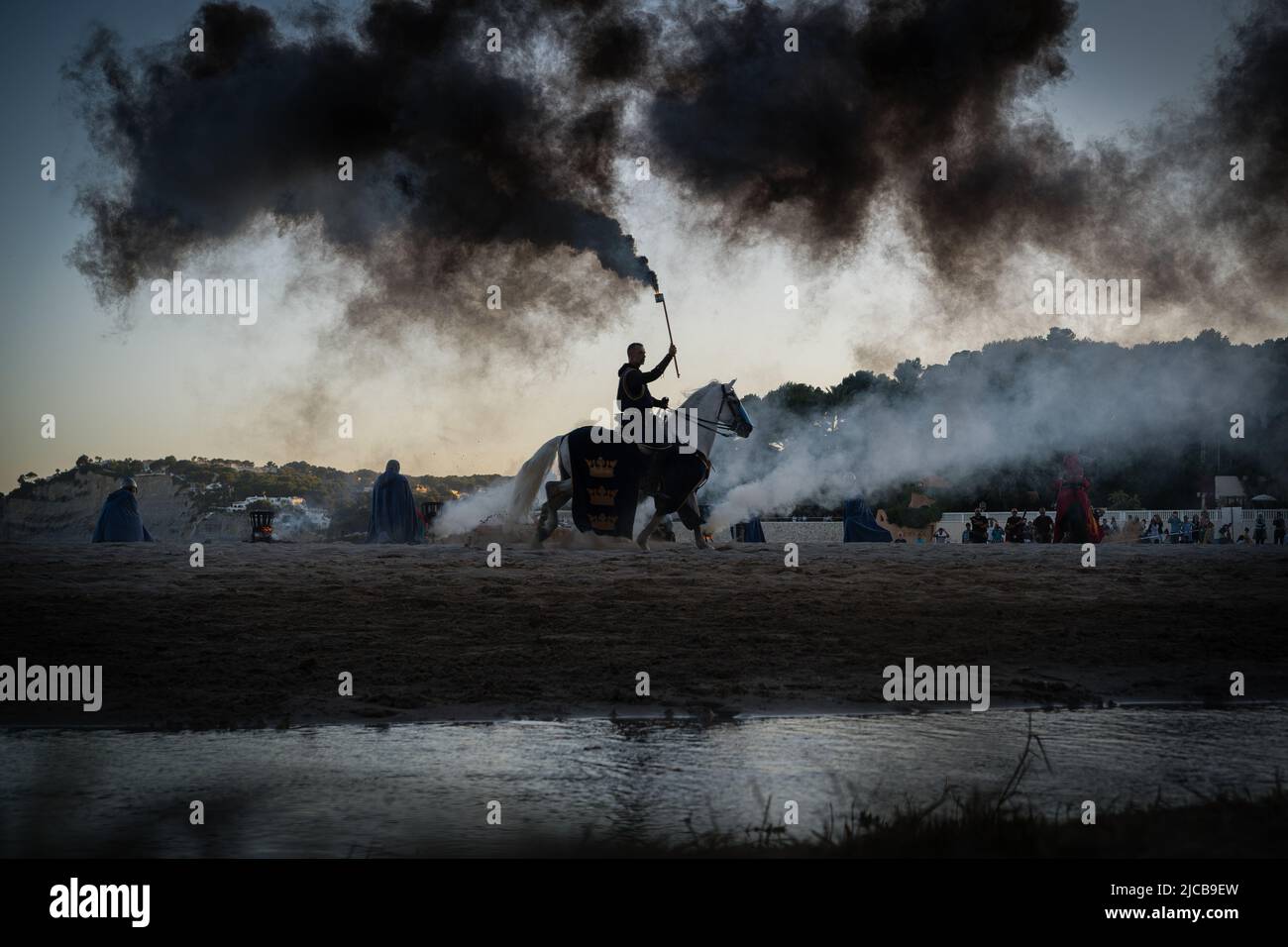 Un partecipante ha visto sul suo cavallo danzante mentre tiene un fumo fiammante durante la tradizione di Mori e cristiani sulla spiaggia di l'ampolla. Secondo giorno della tradizionale festa dei "mori e cristiani" a Teulada Moraira, Alicante, celebrata di nuovo dopo due anni a causa delle restrizioni della pandemia. Secondo la tradizione, queste festività commemorano le battaglie combattute durante la Reconquista, in cui i cristiani dei regni di Spagna conquistarono i domini occupati dai musulmani. (Foto di Diego Radames/SOPA Images/Sipa USA) Foto Stock