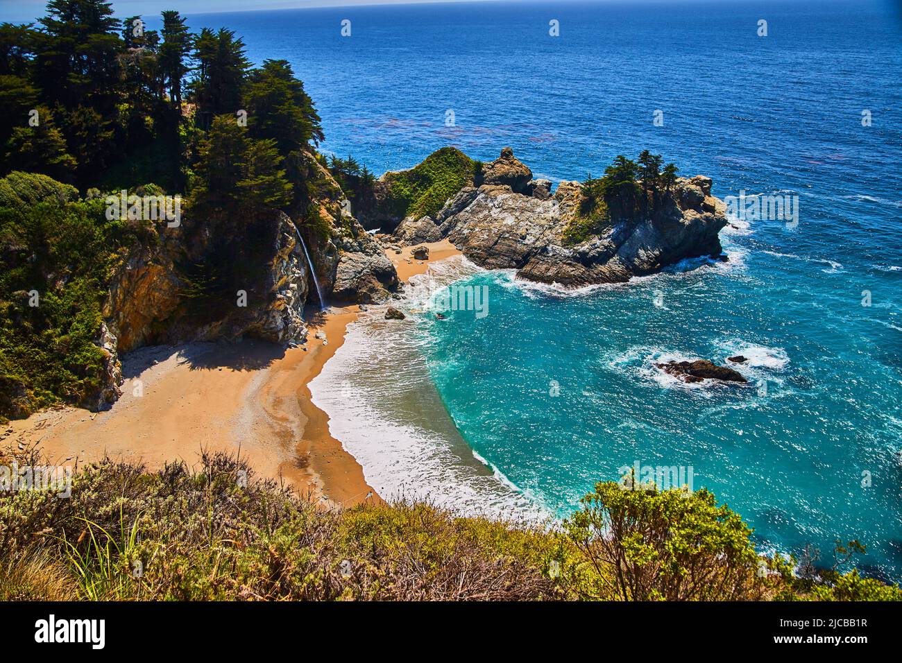 Spiagge di sabbia e rocce costiere circondano cascata nascosta in questa baia dell'oceano Foto Stock