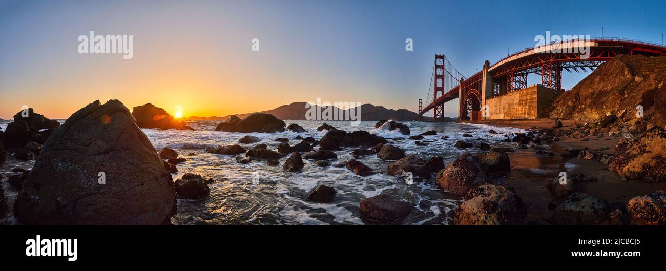 Panorama mozzafiato del Golden Gate Bridge sulla costa dell'oceano con rocce e tramonto Foto Stock
