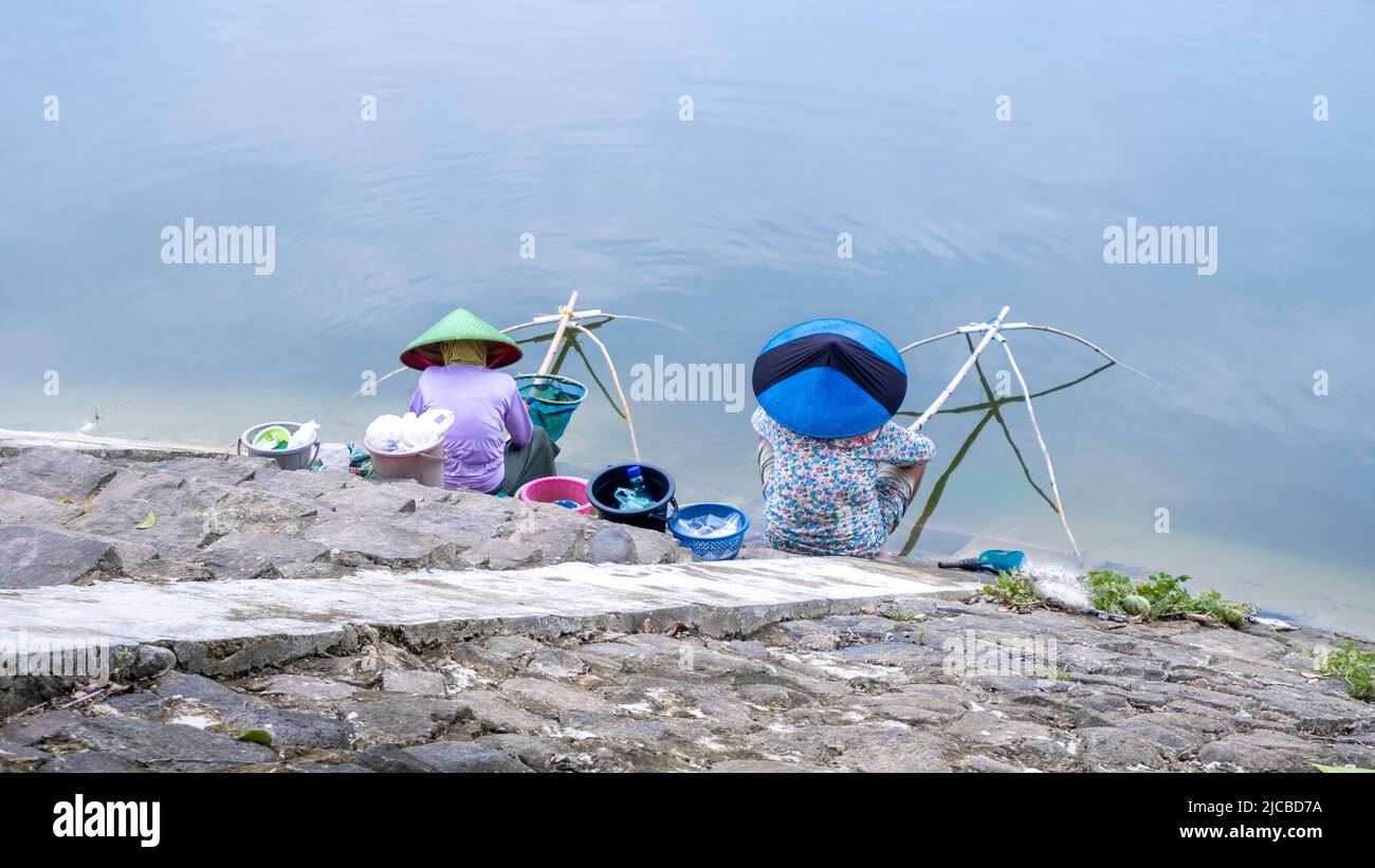 Due pescatori femminili stanno catturando il pesce vicino al lago in acqua blu. Di solito catturano anche i pesci nei fiumi e nei bacini Foto Stock