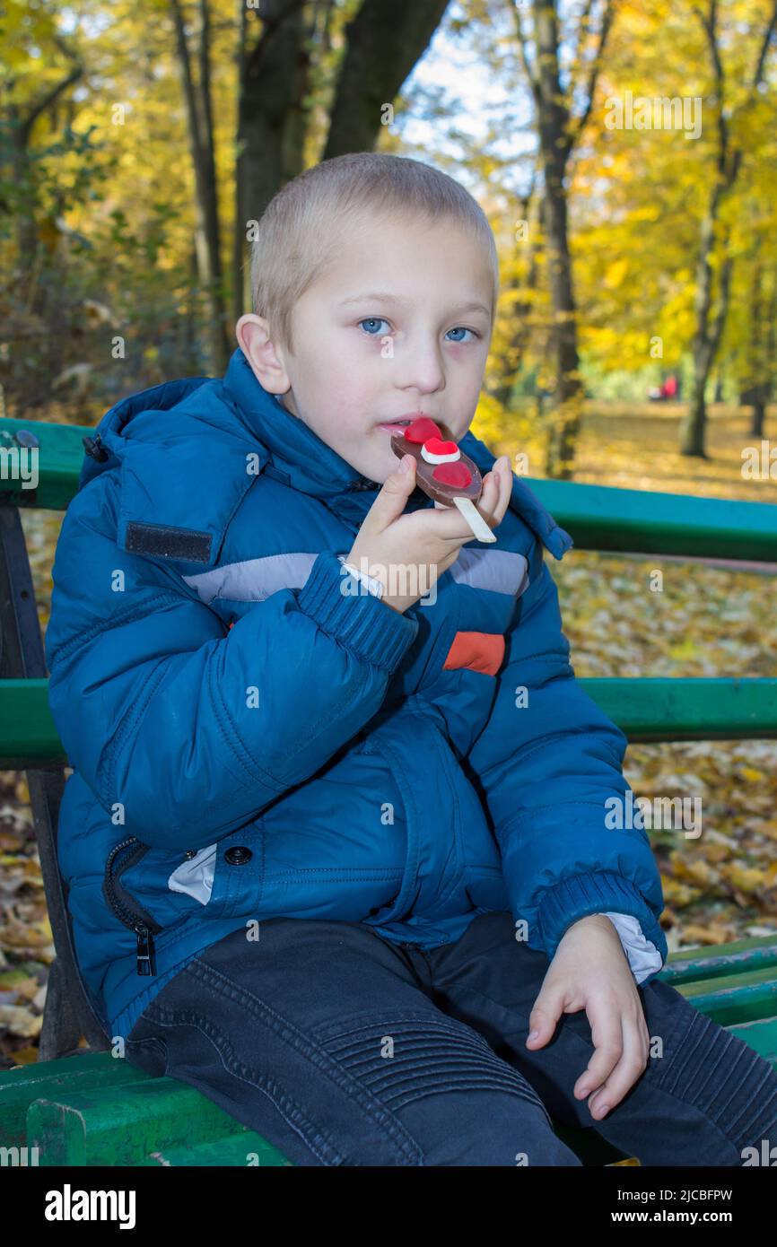 Adorabile ragazzino, mangiando la barra di cioccolato autunno nel parco Foto Stock