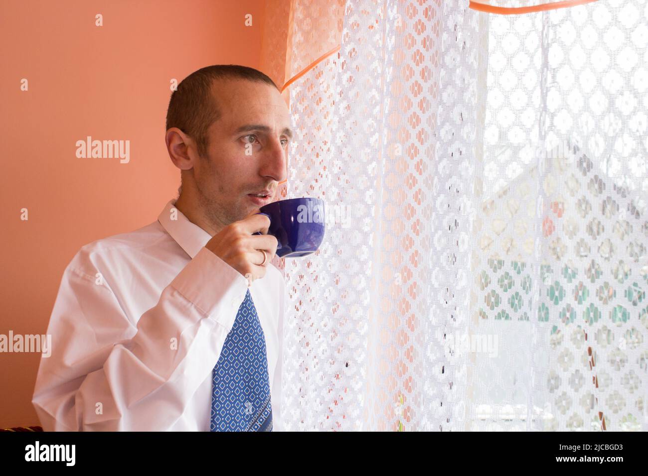 uomo d'affari sicuro che beve il caffè e guarda fuori dalla finestra Foto Stock