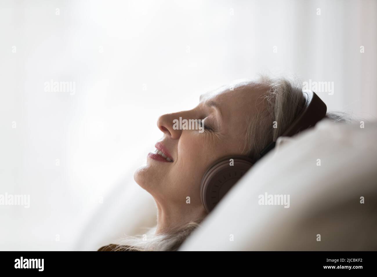 Donna sognante di mezza età in cuffie rilassante sul divano Foto Stock