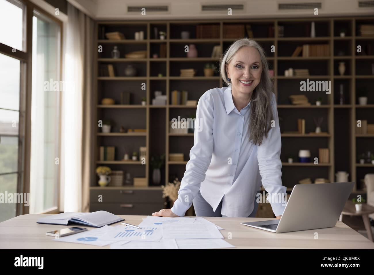 Una donna d'affari sorridente e attraente di successo che si pone sul posto di lavoro Foto Stock