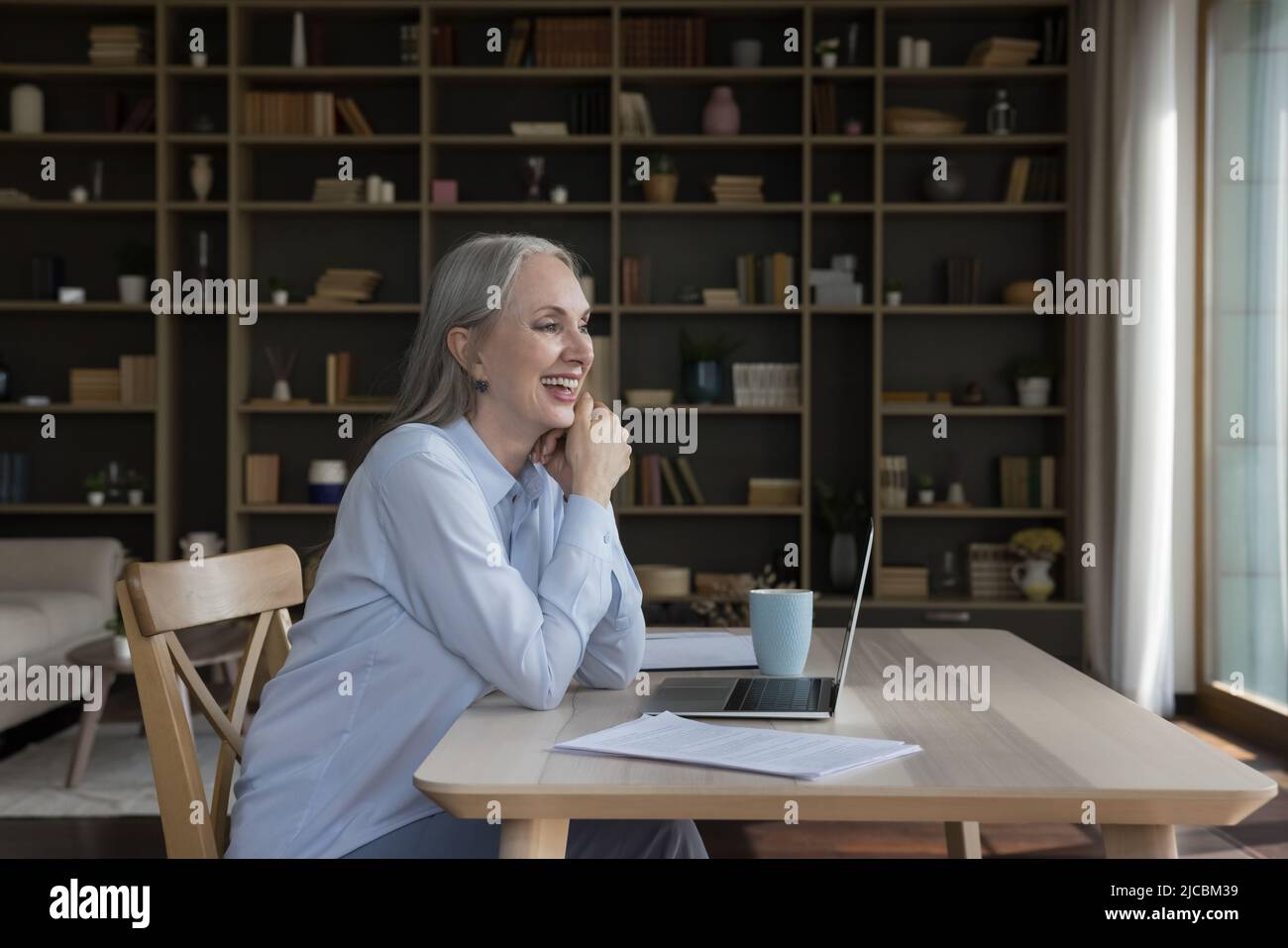 Una donna d'affari più anziana ottimista e felice si siede alla scrivania fissando a distanza Foto Stock