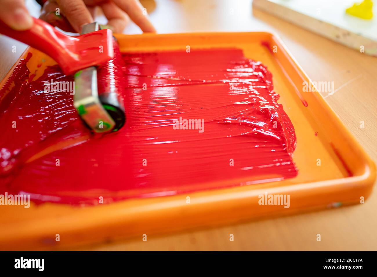 Rotolo di vernice rossa preparato in un vassoio nella mano di un operaio prima della pittura Foto Stock