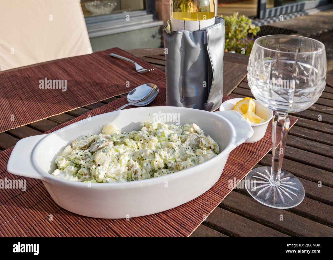 Insalata di patate con bottiglia di vino bianco in manica e bicchiere di vino di cristallo per pasti all'aperto sul tavolo del patio al sole Foto Stock