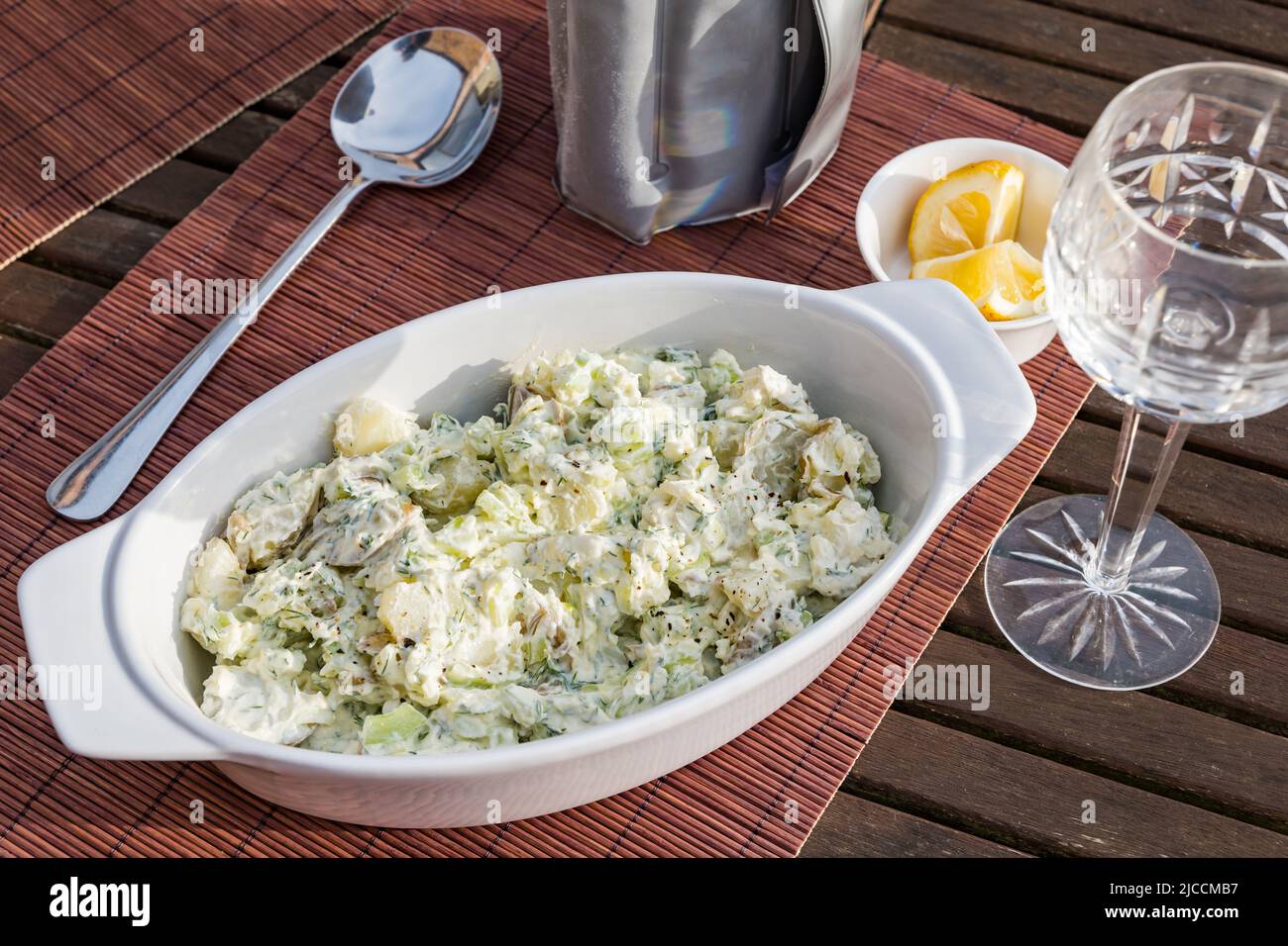 Ciotola di insalata di patate con bicchiere di vino di cristallo per pasti all'aperto sul tavolo del patio al sole Foto Stock
