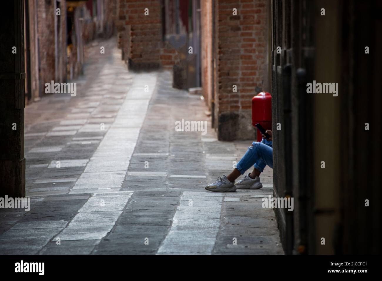 Gambe di un adulto seduto a terra su una strada pedonale vuota Foto Stock