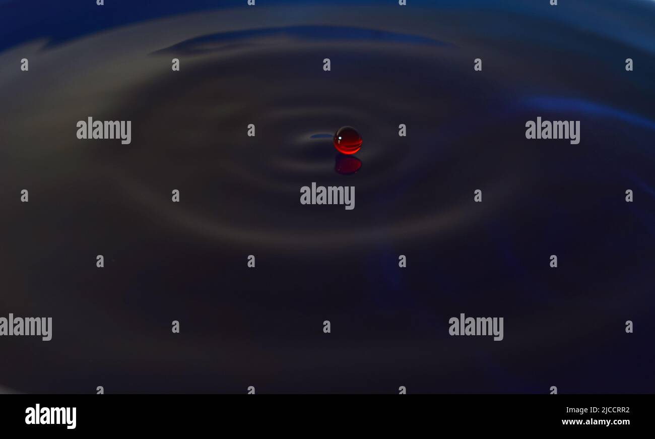 Water drop Fotografia, primo piano di gocce d'acqua rossa in acqua di colore blu scuro. Foto Stock