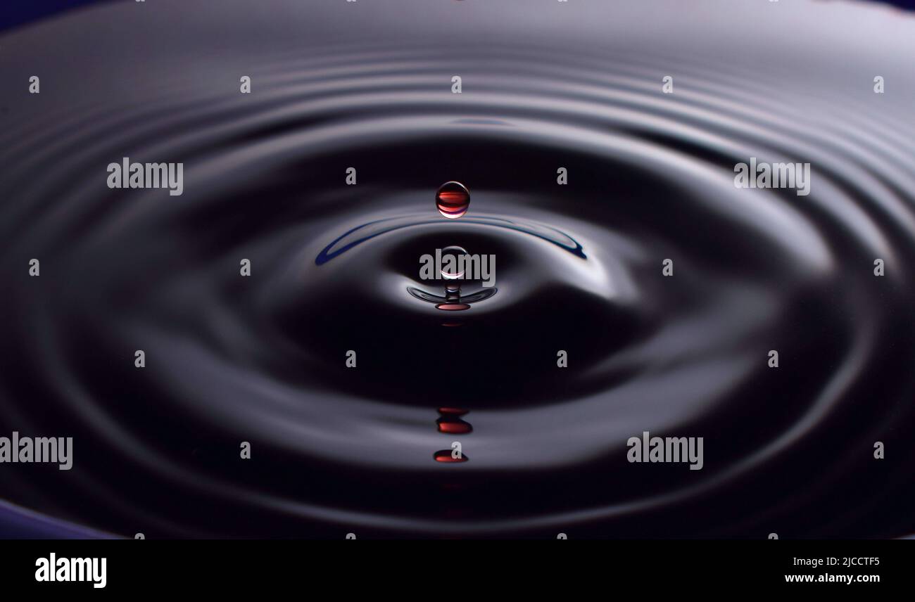 Water drop Fotografia, primo piano di gocce d'acqua rossa in acqua di colore blu scuro. Foto Stock