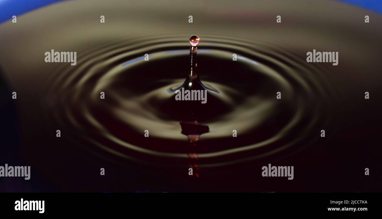 Water drop Fotografia, primo piano di gocce d'acqua rossa in acqua di colore blu scuro. Foto Stock