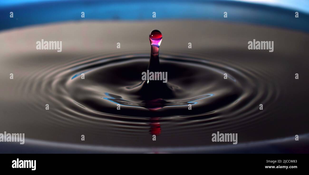 Water drop Fotografia, primo piano di gocce d'acqua rossa in acqua di colore blu scuro. Foto Stock