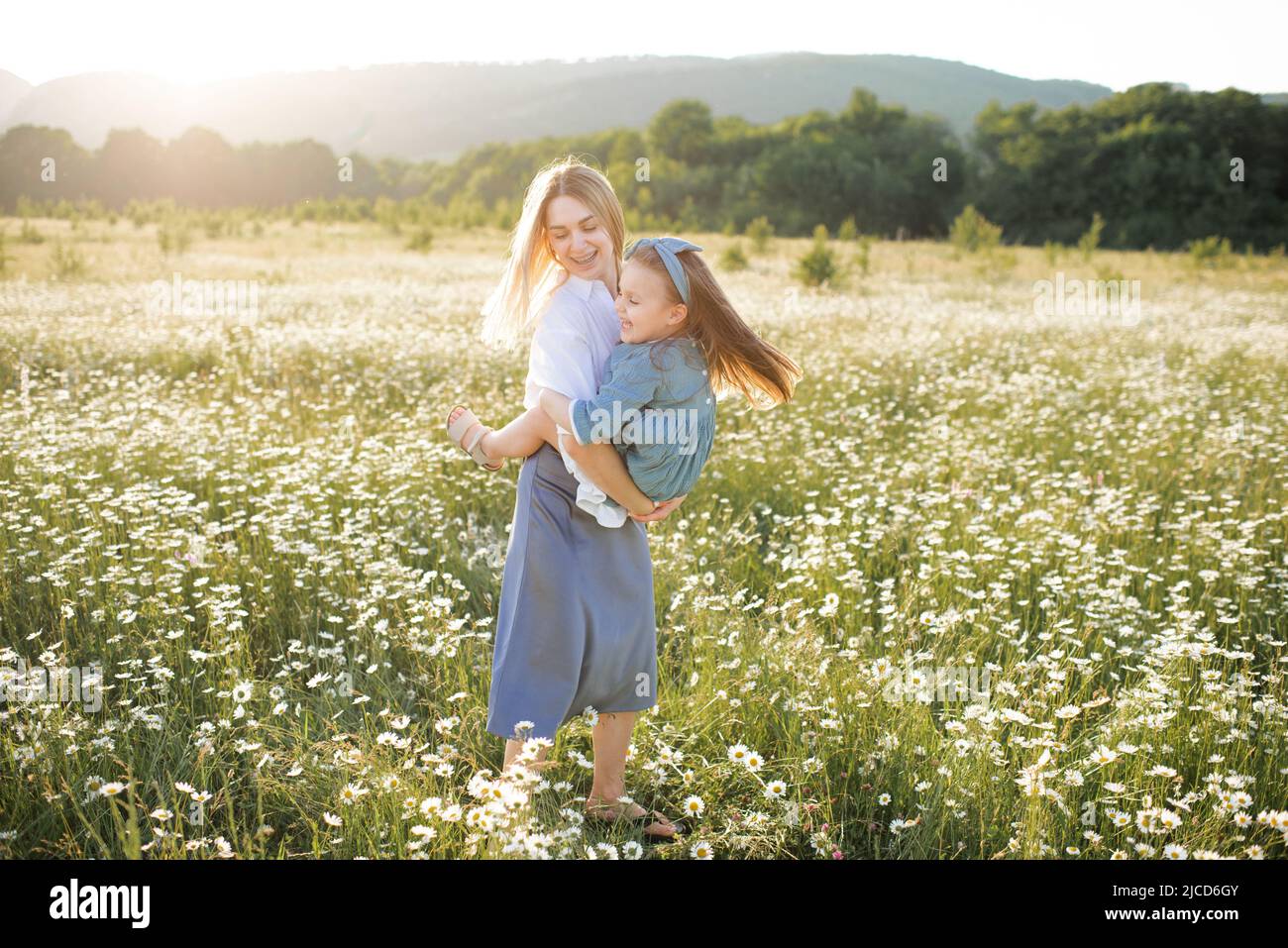 Bella ragazza carina che tiene le mani e giocare con bambina a piedi in campo camomilla con fiori in fiore sullo sfondo della natura. Famiglia Foto Stock