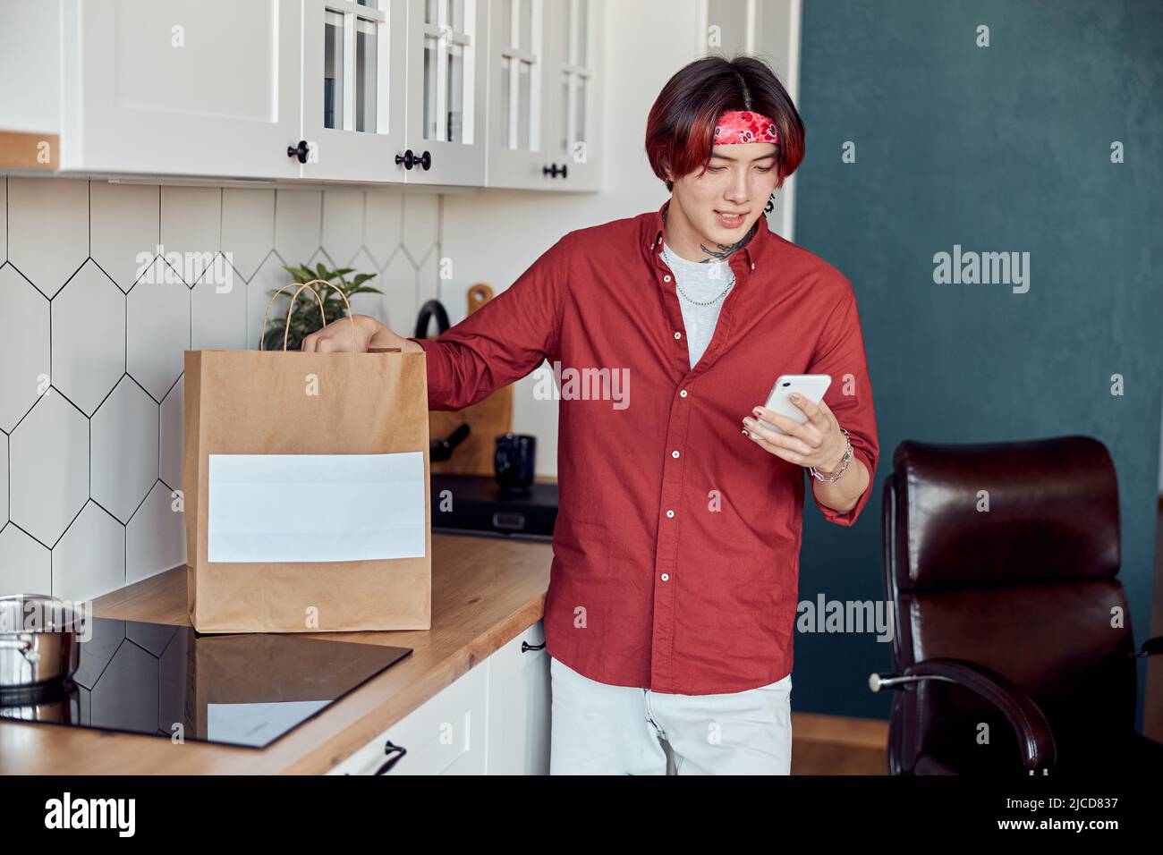 Sorridente ragazzo asiatico che tiene lo smartphone durante la consegna di cibo Foto Stock