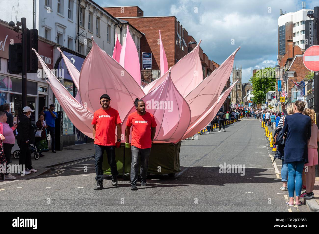 La Grand Parade al Victoria Day, un evento annuale ad Aldershot, Hampshire, Inghilterra, Regno Unito. Nutkhut artisti di performance con un fiore gigante di loto Foto Stock