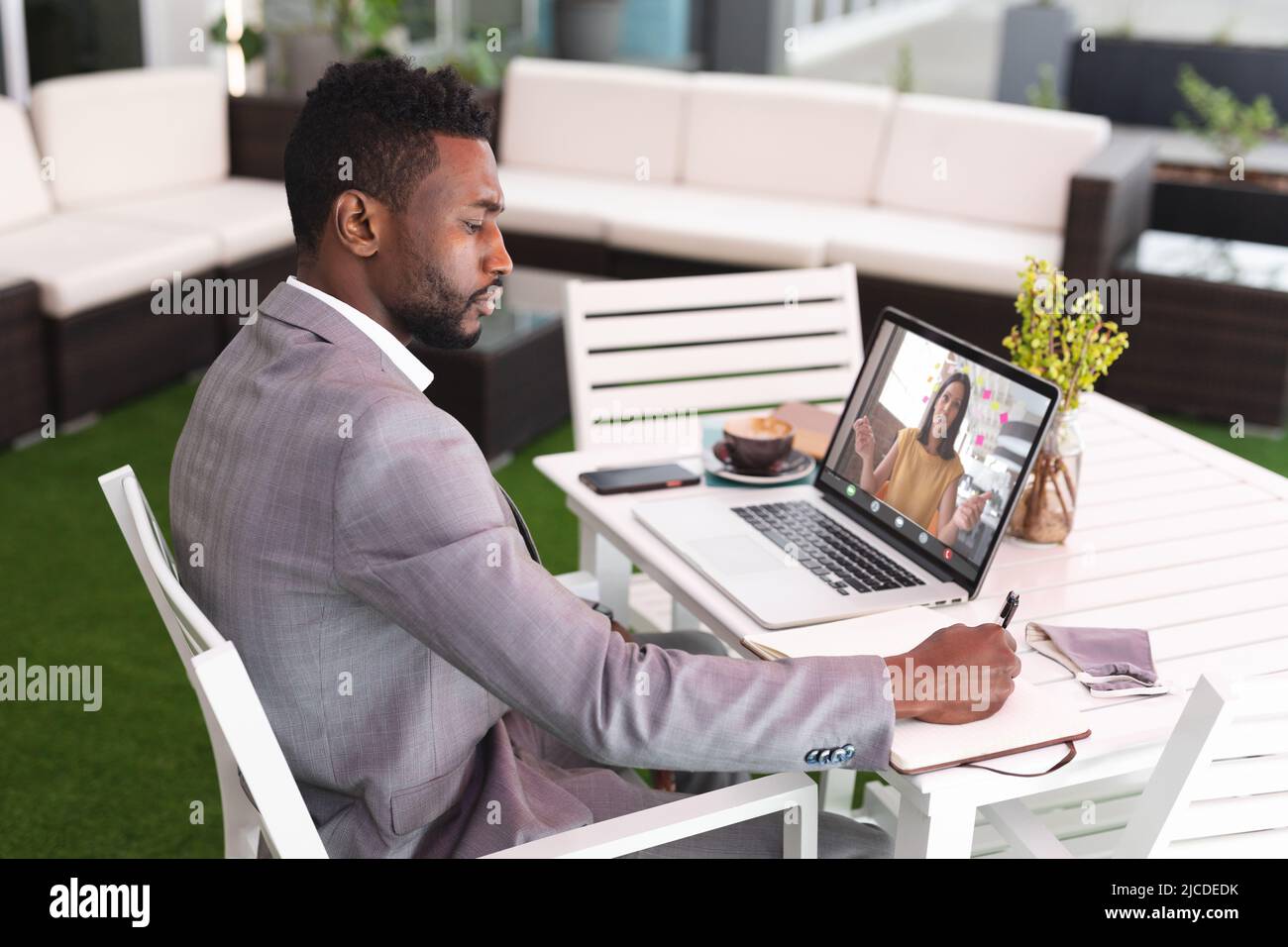 Un uomo d'affari afroamericano che scrive in agenda mentre videoconferenze con un collega su un laptop Foto Stock