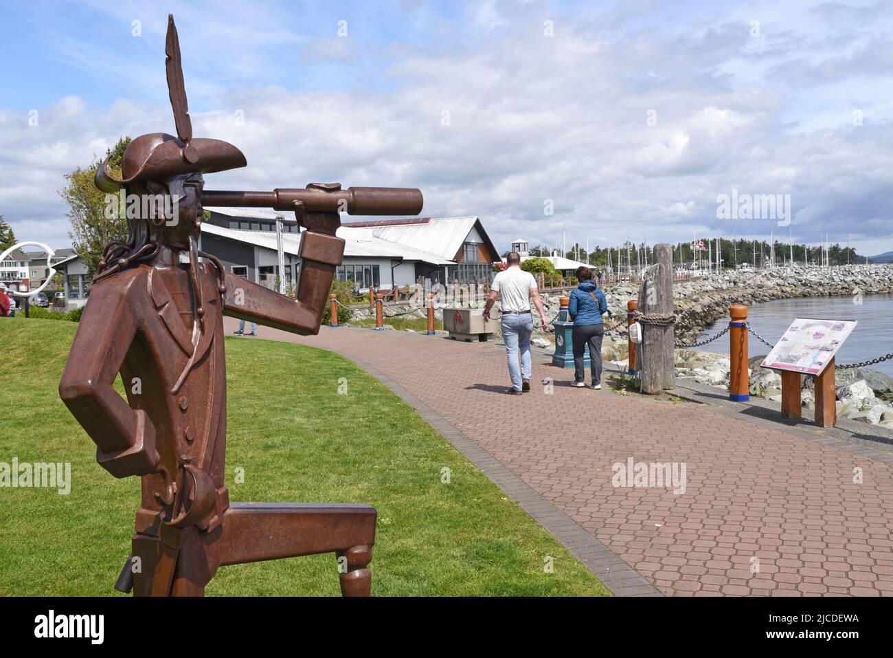 Una vista di una scultura di un pirata con un telescopio e il porto e il porto turistico a Sidney, British Columbia sull'isola di Vancouver, Canada. Foto Stock