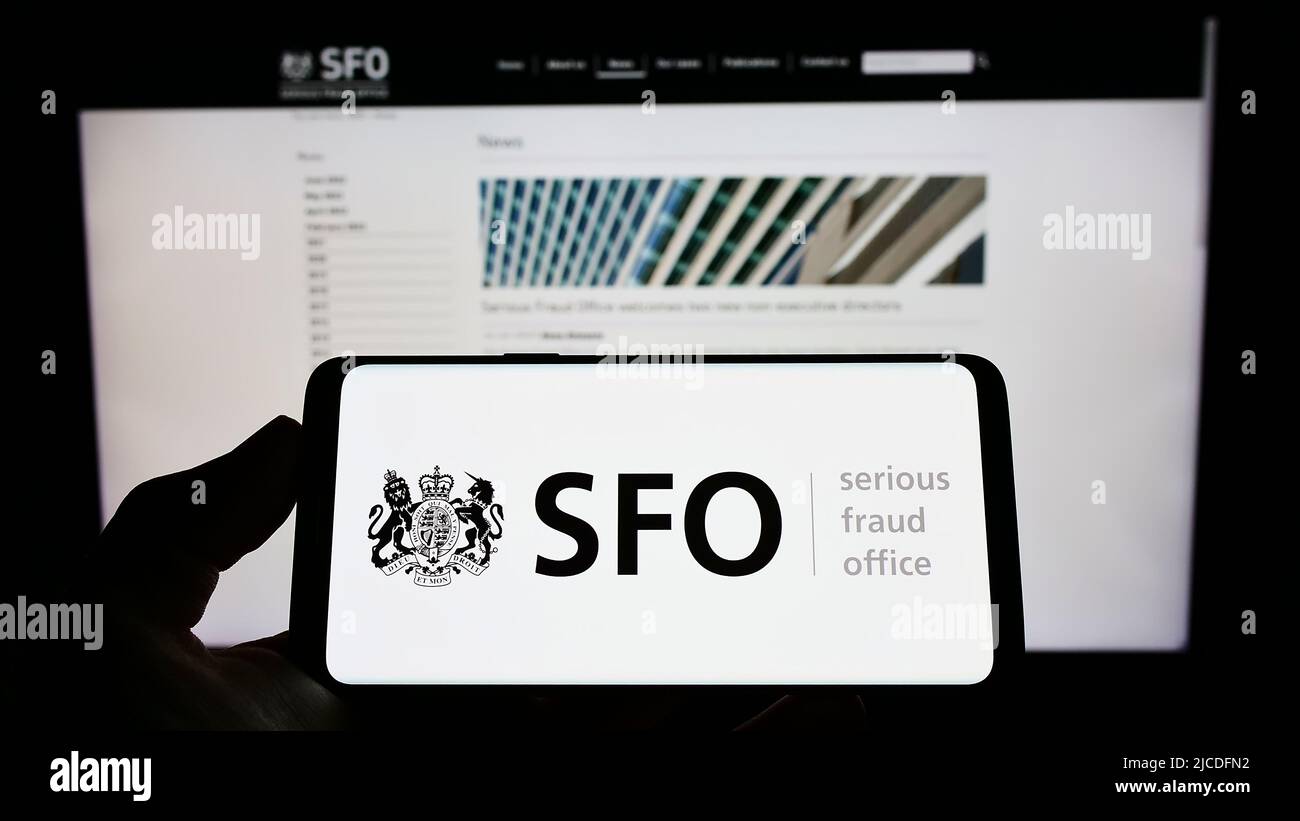 Persona che tiene il cellulare con il logo dell'agenzia britannica Serious Fraud Office (OFS) sullo schermo di fronte alla pagina web. Mettere a fuoco sul display del telefono. Foto Stock