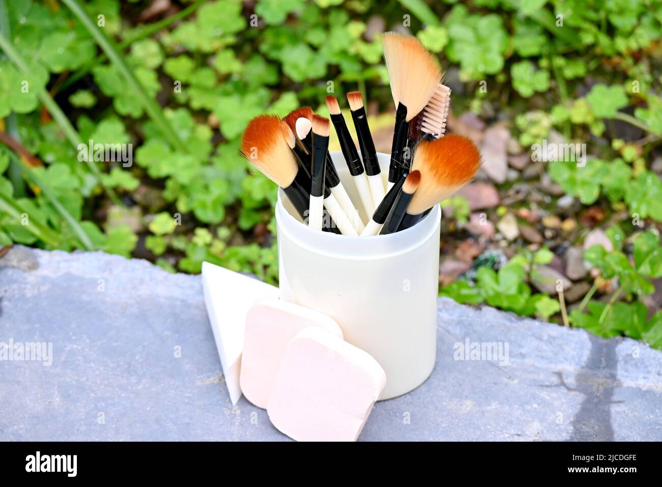 closeup il mazzo bianco marrone makeup kit spazzola con spugne palla nella scatola di plastica su sfondo verde marrone fuori fuoco. Foto Stock