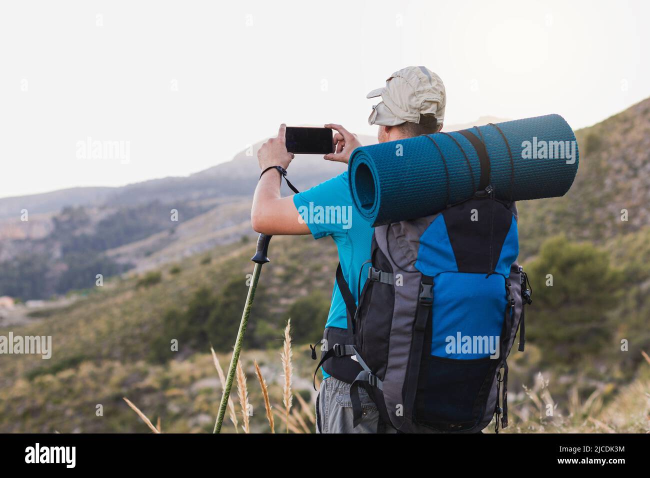 Un escursionista irriconoscibile, adulto, maschio, caucasico, con uno zaino, Stuoia, pali, vestito con una T-shirt blu, cappuccio e pantaloni grigi è sulla montagna prendere Foto Stock