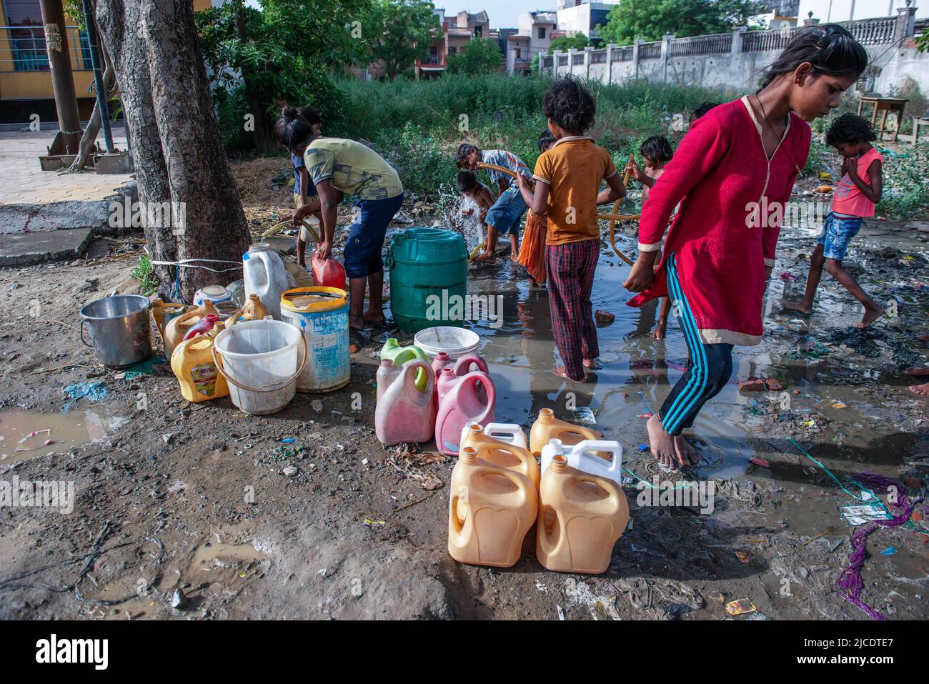 I bambini delle slum riempiono i loro contenitori con acqua da una perdita di condutture di acqua di strada in Ghaziabad. I bambini delle slum raccolgono l'acqua potabile e l'uso quotidiano da una perdita del tubo dell'acqua di bordo della strada. Foto Stock