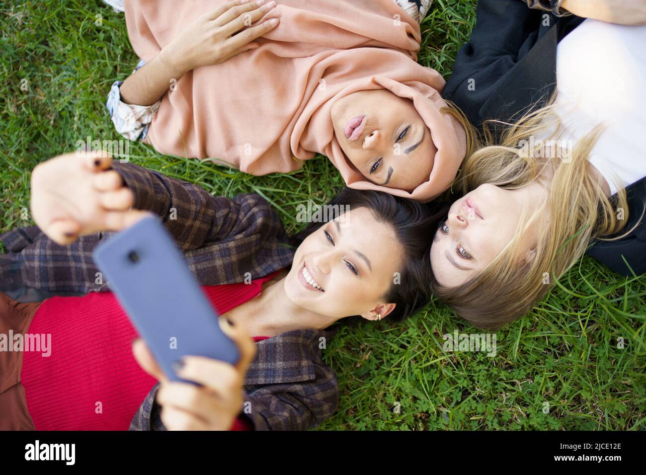 Fidanzate multirazziale che giacciono in cerchio e prendono selfie Foto Stock